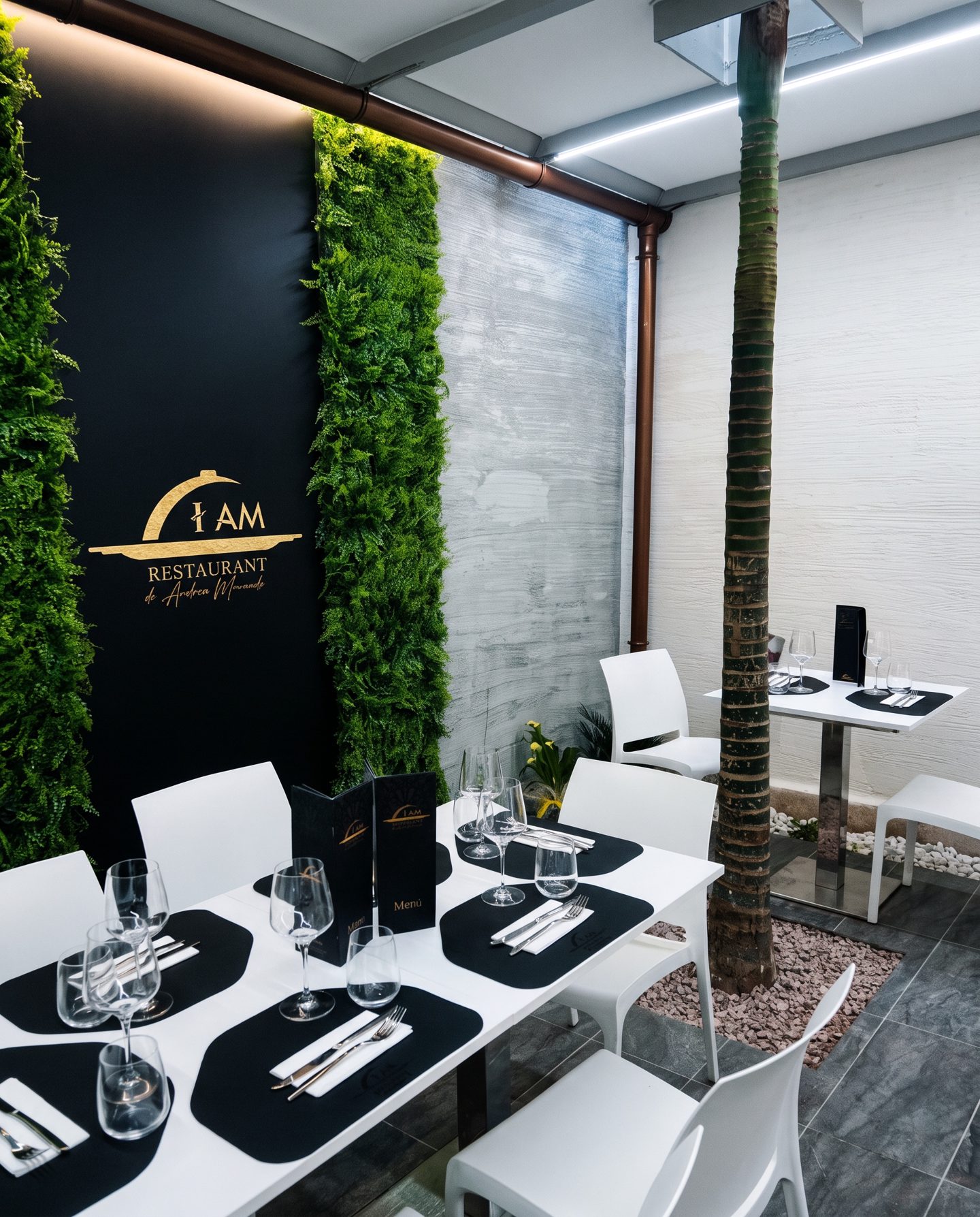 La sala di I Am Restaurant: la parete nera con l'insegna dorata, due pareti di felci e la palma al centro.